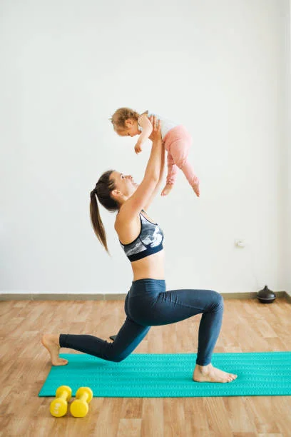 Jeune maman en fente avant, tenant son bébé levé au-dessus d'elle, lors d'une séance de gym postnatale